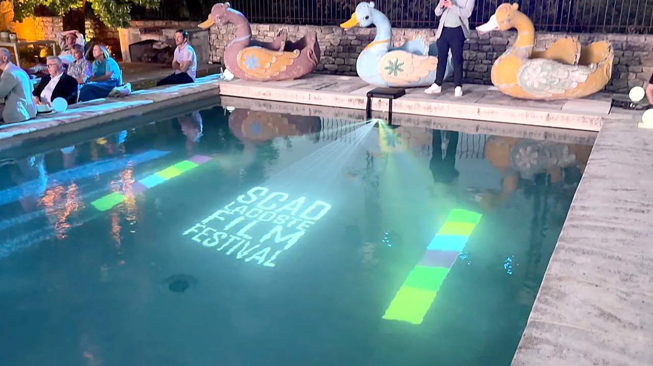 Guests around a garden pool at night while a Pool-On projector projects coloured light under the water