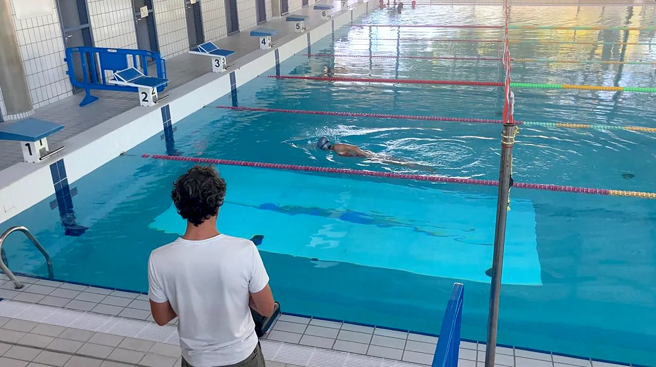 A coach watches a swimmer follow a projected pacer in a lane
