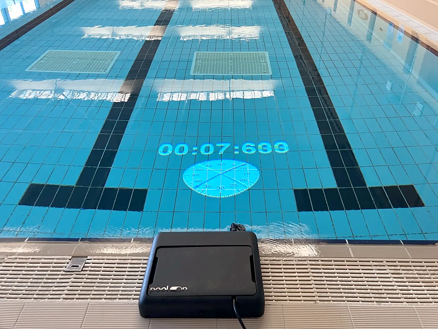 A projected race timer on a pool lane, next to the Pool-On projector
