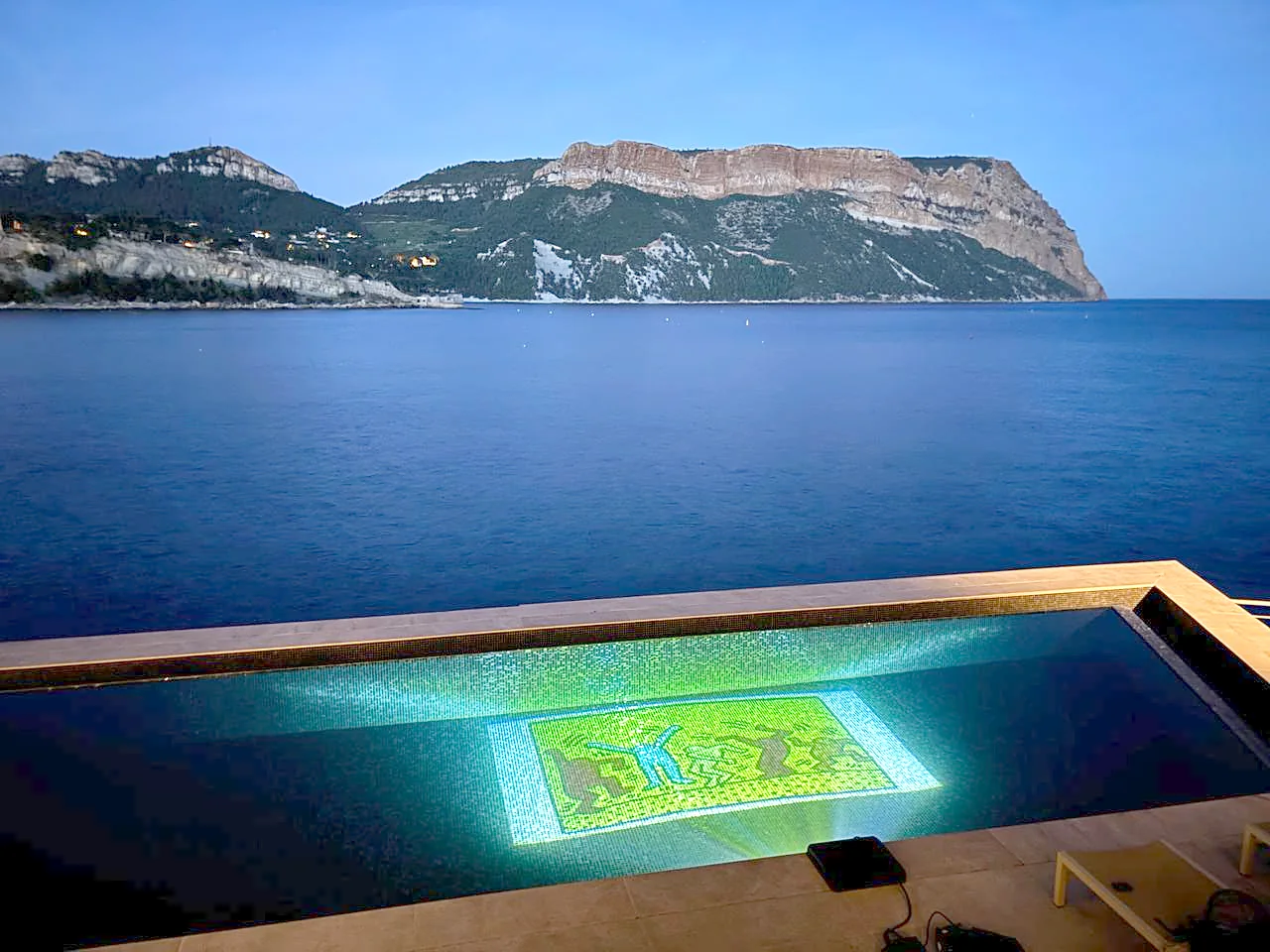 A Pool-On projector projecting a Keith Haring artwork into an infinity pool overlooking the sea at dusk